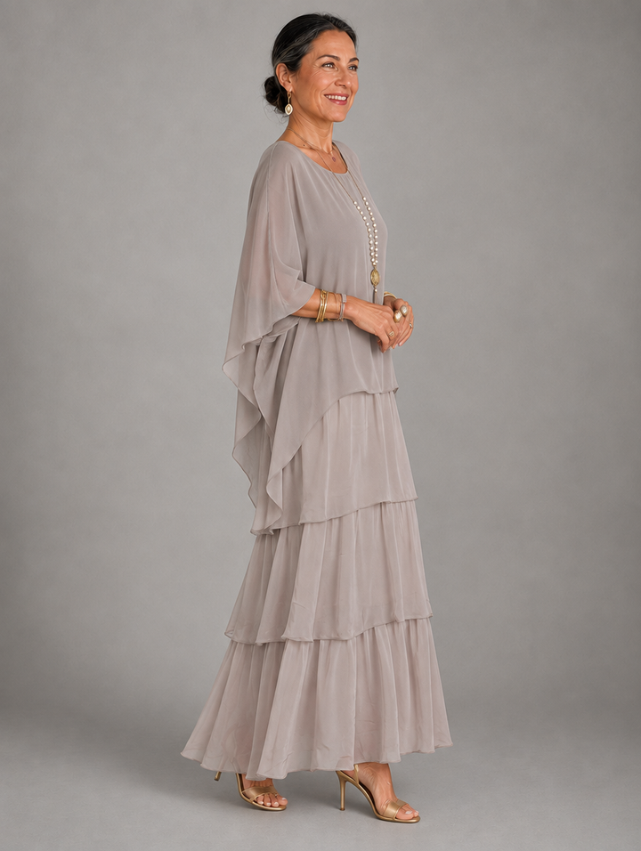 Side view of the taupe tiered chiffon maxi dress with a flowing cape sleeve and stacked skirt tiers