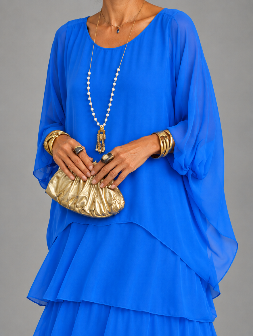 Torso close-up of the royal blue dress, showing the loose sheer sleeves and layered hem, with the model holding a gold clutch. 27