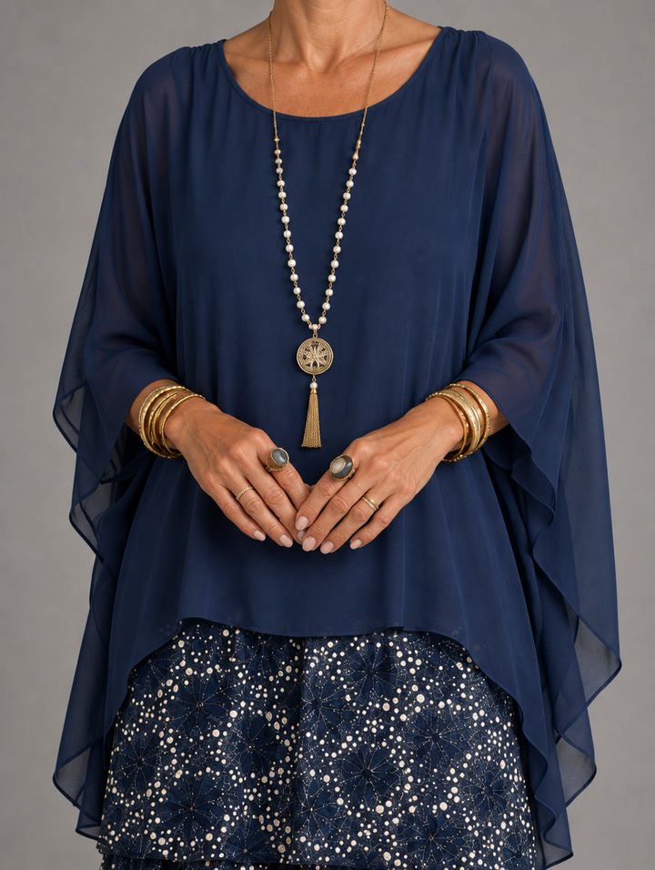 Close-up of the navy chiffon overlay with draped batwing sleeves, worn with a pearl and gold pendant necklace over the dotted tiered skirt. 45