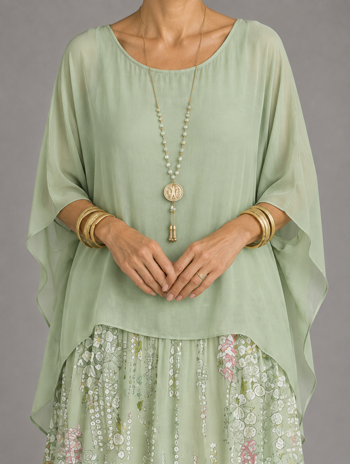 Close-up of the sage green sheer chiffon overlay with wide draped sleeves, styled with a beaded gold pendant necklace and bangles over the floral skirt. 48