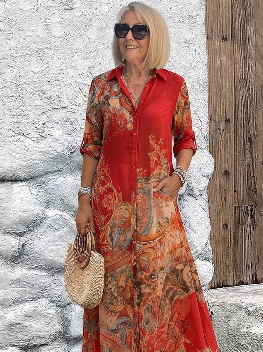 Button-front maxi dress in bright red with orange and teal scrolling print, worn by a smiling model with a straw handbag. 3