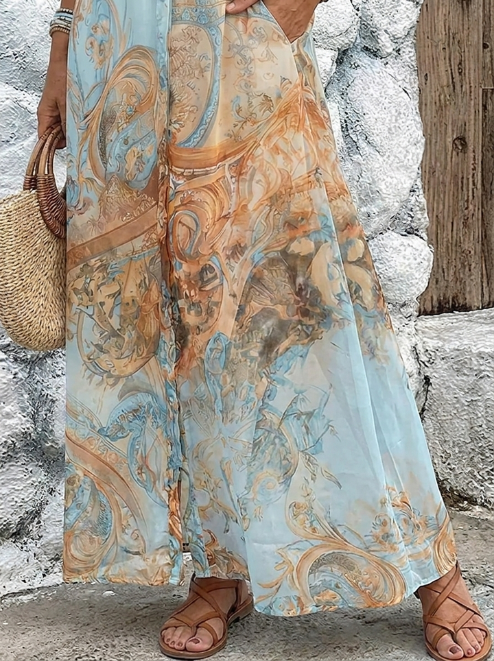 Close-up of the flowing light blue chiffon skirt with orange ornate print, shown with brown strappy sandals and a straw bag. 6