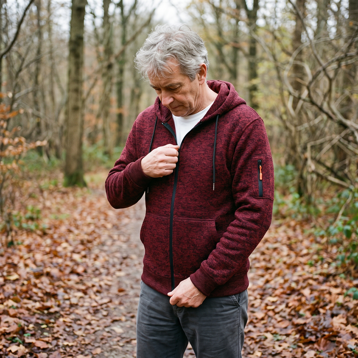 Man in a burgundy hoodie over a white tee, zipping it up on a leafy forest path 6