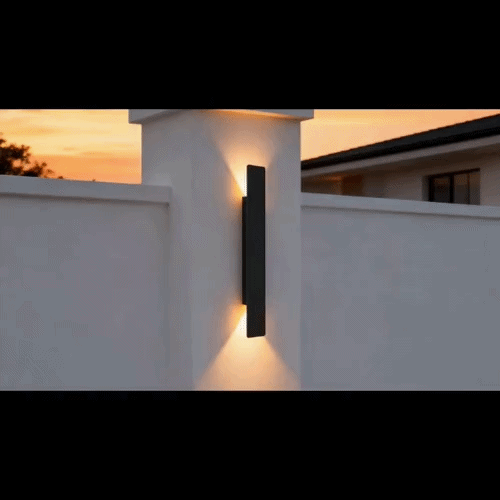 Black wall light on a gate pillar with warm beams on the stucco above and below.