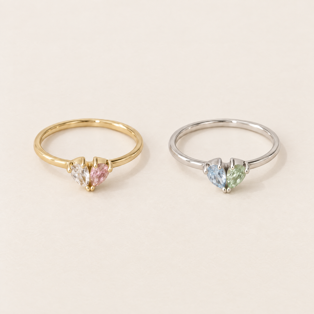 another view of two heart rings, one gold-toned with clear and pink stones and one silver-toned with light blue and pale green stones.