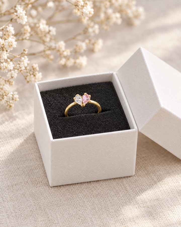 detail of the gold-toned heart ring with clear and pink stones in an open white gift box.