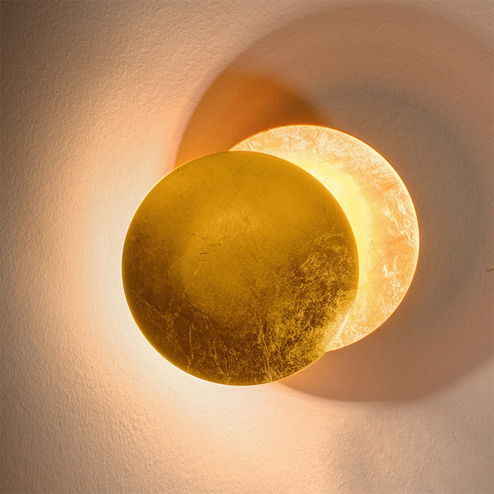 Detailed close-up of the gold-leaf textured front disc overlapping the glowing back disc on a plaster wall 11