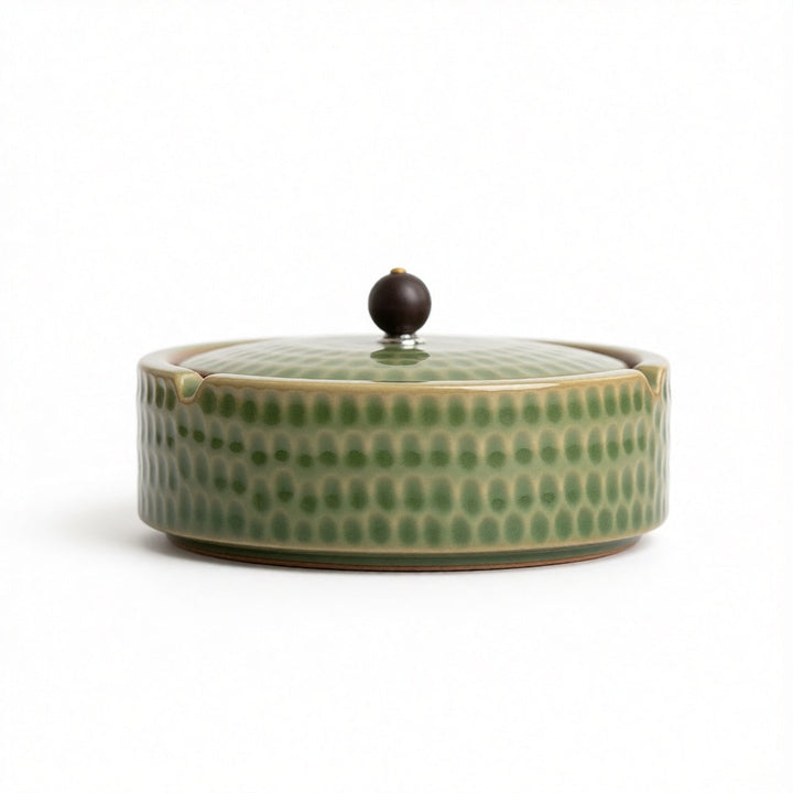 Side view of a light sage green glazed ashtray with the lid on and a dark round knob.