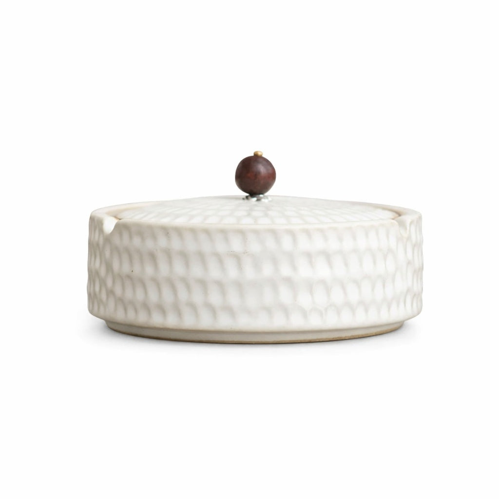 Side view of a cream-white matte ashtray with the lid on and a reddish-brown wooden knob.