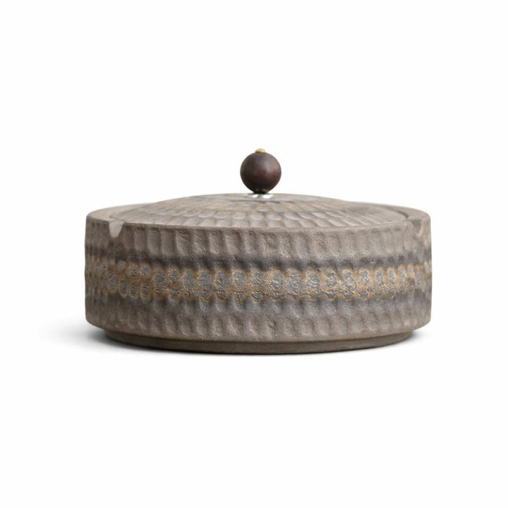 Side view of a gray-brown rustic ashtray with the lid on and a dark wooden knob.
