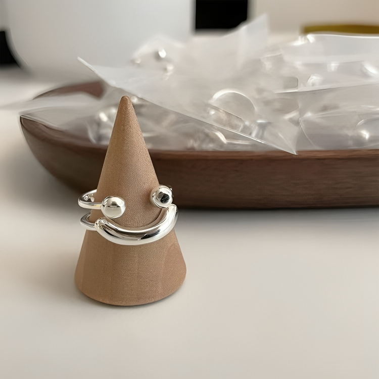Ring displayed on a wooden cone stand, with a wooden dish of small clear bags of rings blurred behind it. 7