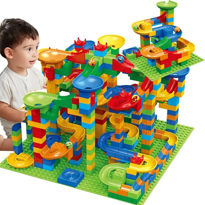 Young boy looks at a tall multicolor marble run building set with funnels and slides built on green baseplates.