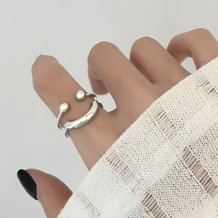Close view of the open double-band ring worn on a finger, with a white knit sleeve and dark nails in the frame. 3