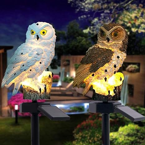 White owl light and brown owl light glowing side by side on stakes with solar panels in a garden at night.
