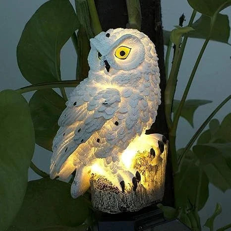 Close-up of a lit white owl light with a yellow eye among large green leaves.