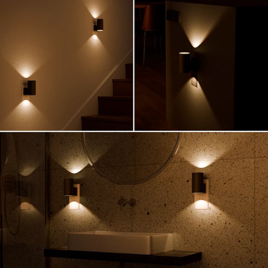 Another view of lamps lighting a staircase, a dark hallway and a bathroom sink area with warm up-and-down beams.