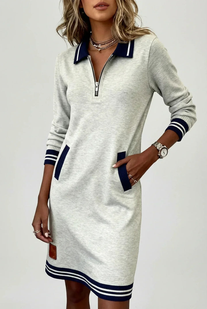 Model in the light gray dress against a plain background, one hand in a pocket, showing the zip neckline and striped hem. 6