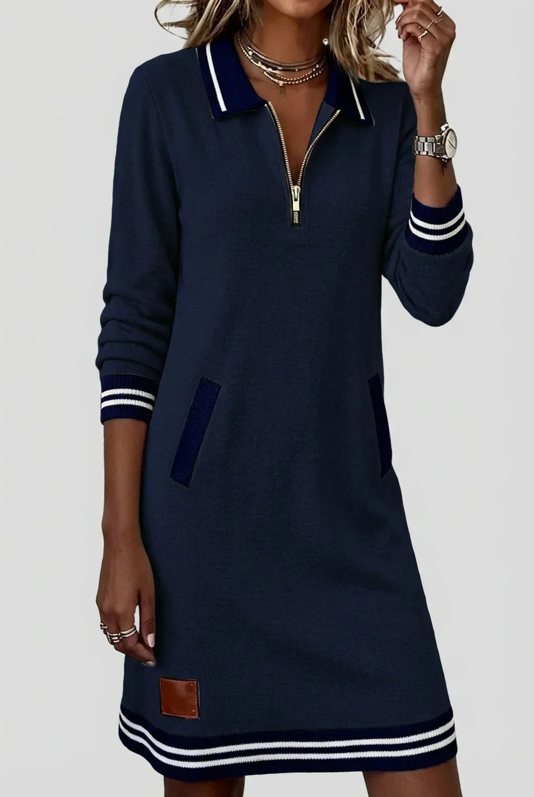 Navy dress worn by a model with one hand at her necklace, showing zip front, ribbed pockets and striped hem. 9