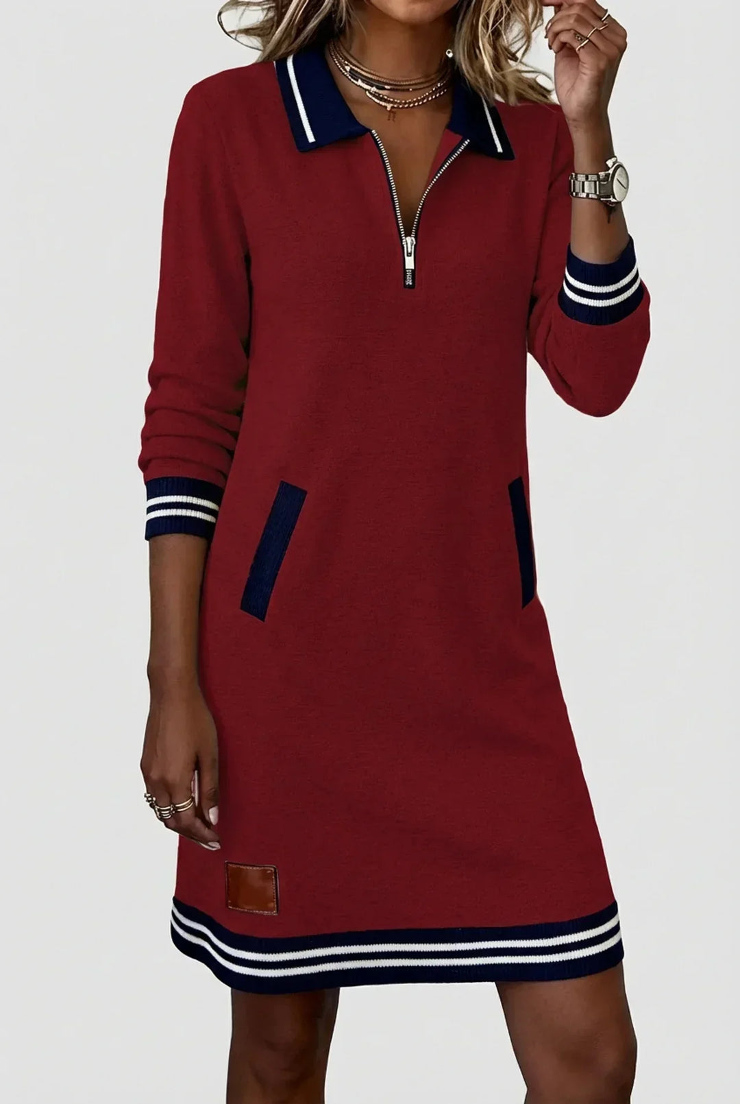 Burgundy dress on a model with hand raised to her necklace, showing zip collar, ribbed pockets and striped hem. 12