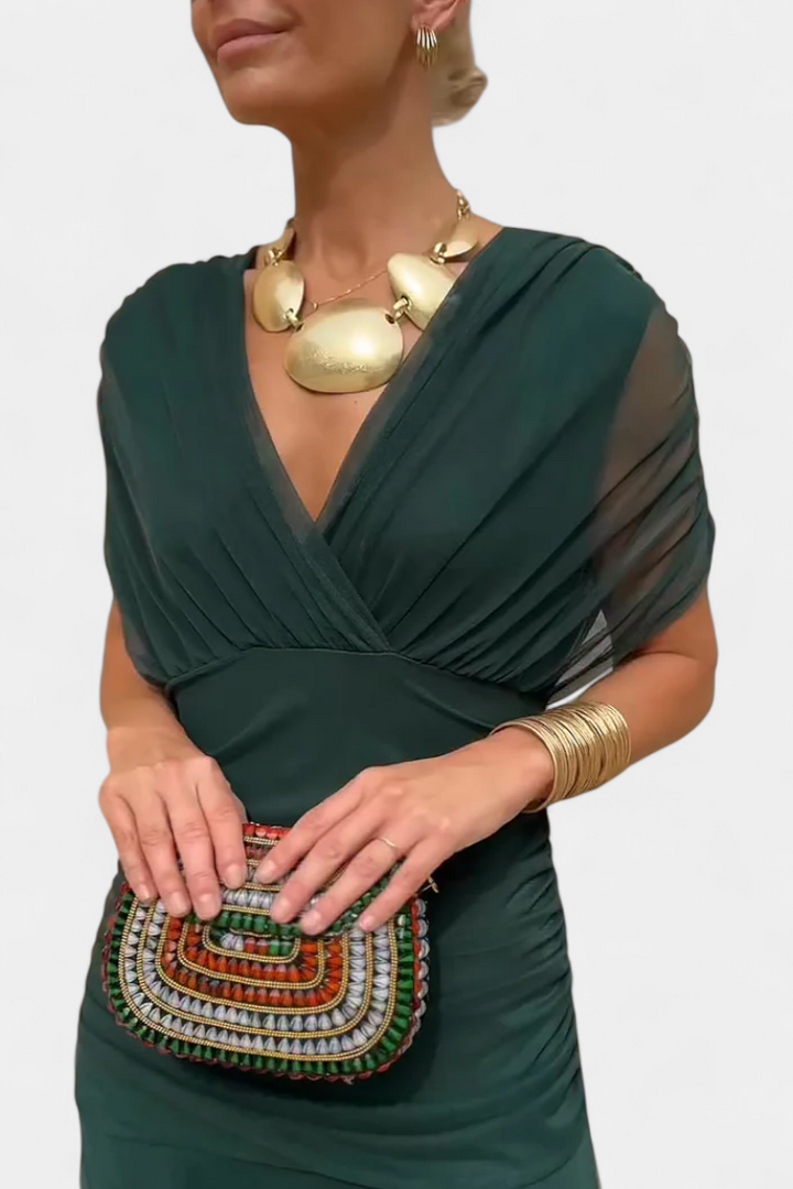 Close-up of the green dress's wrap-style V-neck, sheer cap sleeves and ruched waistband, with a gold statement necklace. 7