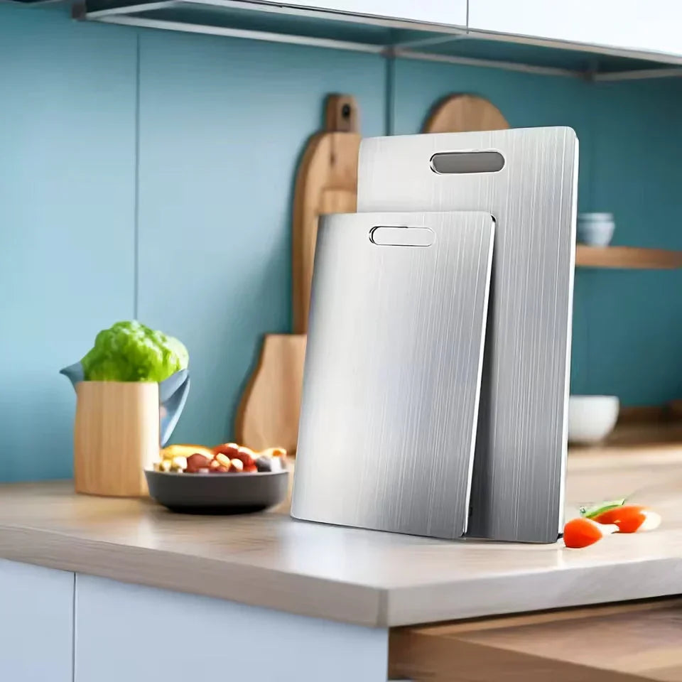 Two metal cutting boards leaning on a kitchen counter against a teal wall, beside a bowl of food, a lettuce head and wooden boards.