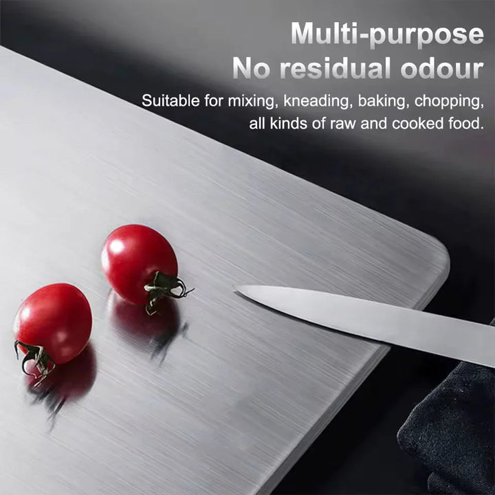 Close-up of the brushed metal board surface with two cherry tomatoes and a knife blade resting on it.