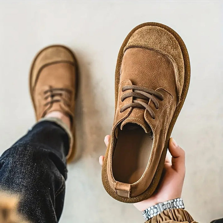 Hand holds a brown leather shoe showing the open collar and stitching.