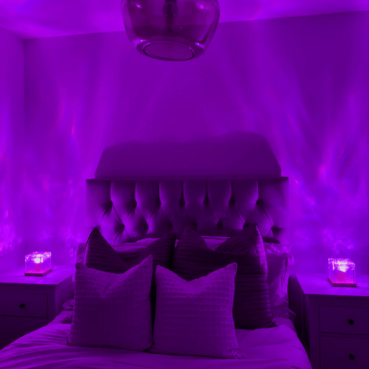 Same bedroom lit in vivid purple, with two cube lamps on the nightstands projecting soft wavy light onto the walls. 3