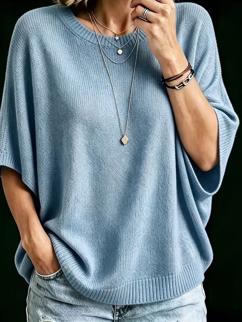 Light blue knit batwing top, close-up front view with hand raised to chin.