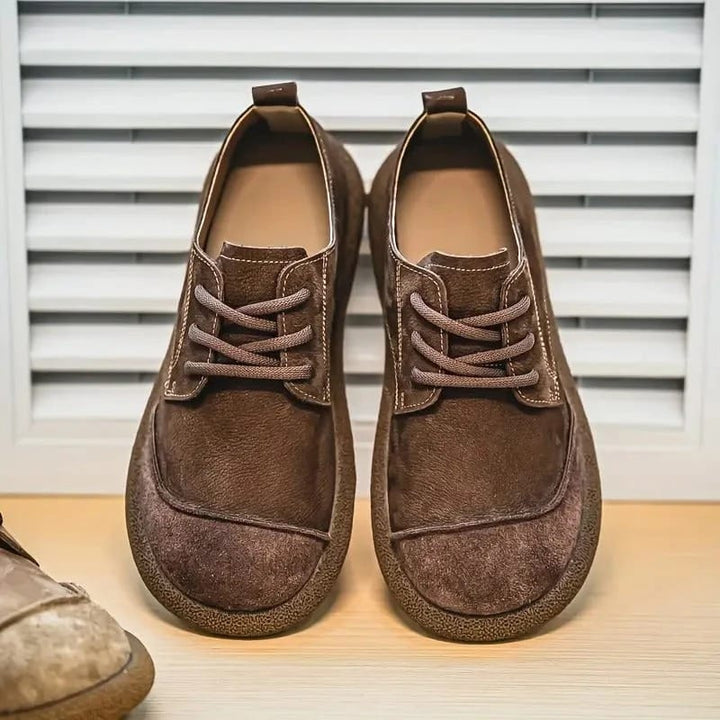 Pair of brown lace-up shoes seen from the front on a wooden shelf by white shutters 6