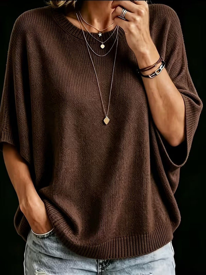 Dark brown knit batwing top, close-up front view with layered necklaces and light jeans.