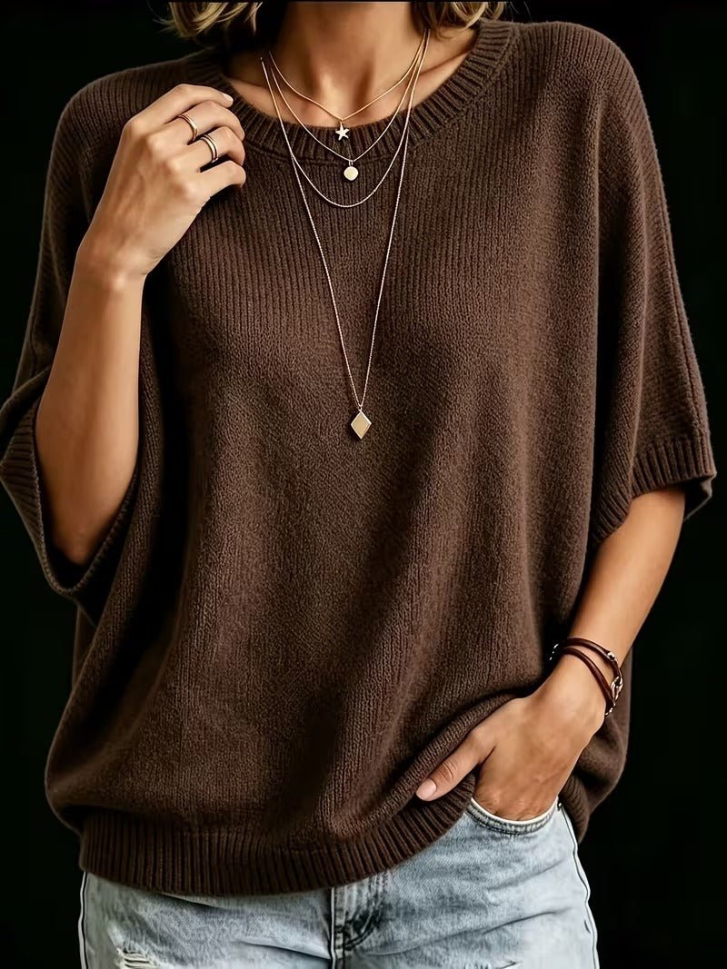 Dark brown knit top worn with one hand on the collar and the other in a jeans pocket, loose batwing sleeves.