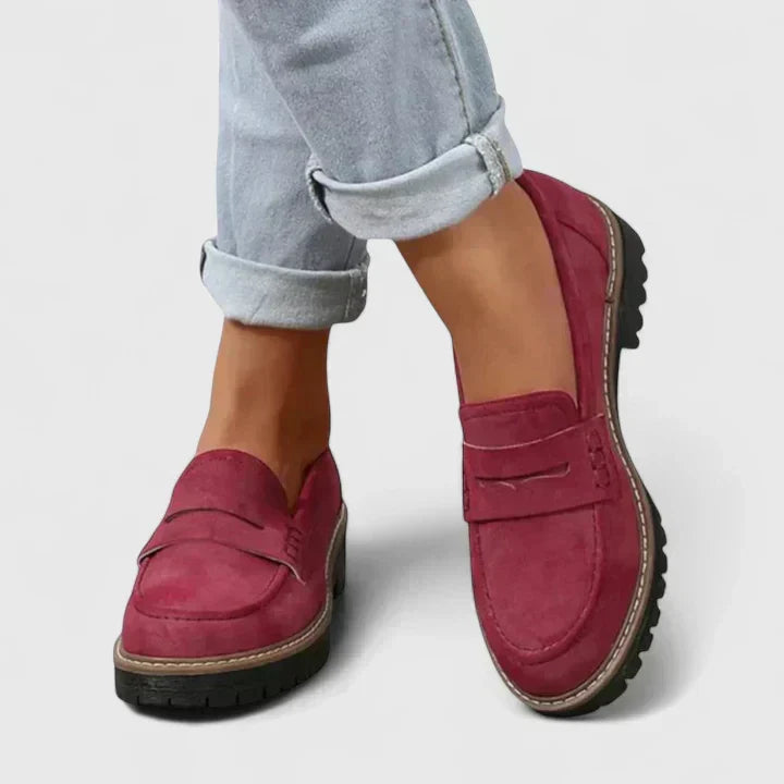 Burgundy red suede-look loafers with low black lugged soles, worn with rolled light gray jeans, detail.