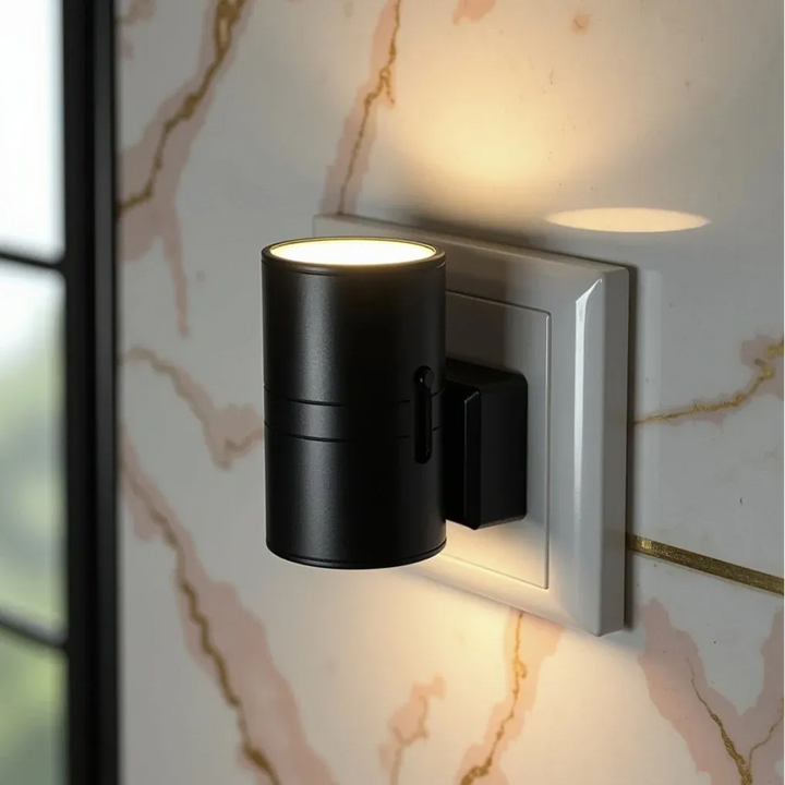 Black cylindrical plug-in night lamp glowing warmly on a wall outlet with pink marble and gold veining.