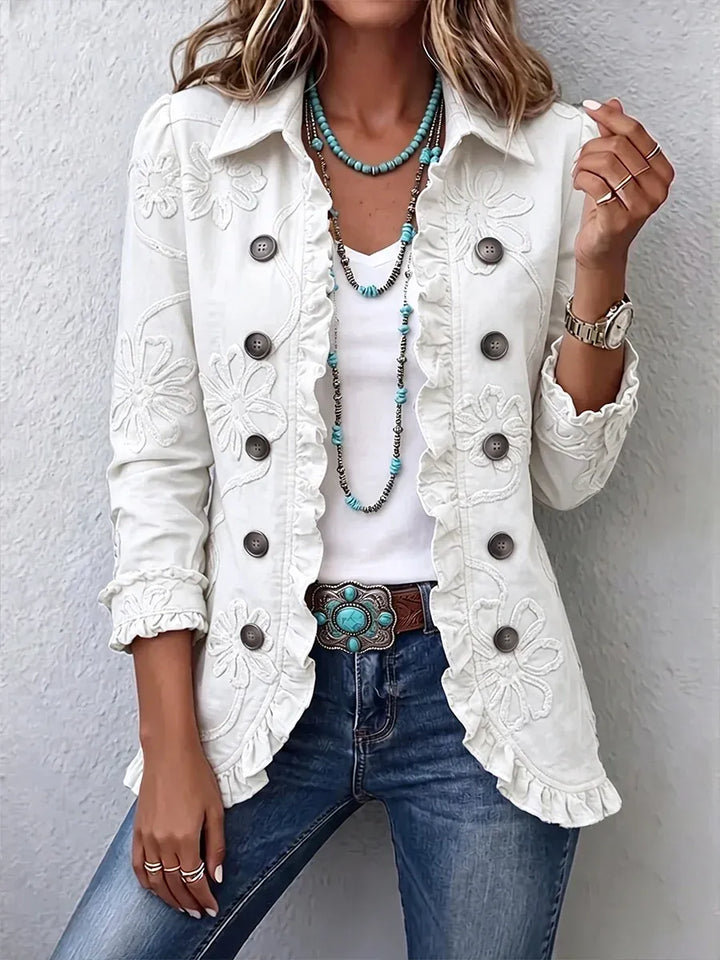 White floral embroidered utility jacket with tonal embroidered flowers and ruffled edges styled with a turquoise belt buckle and jeans.