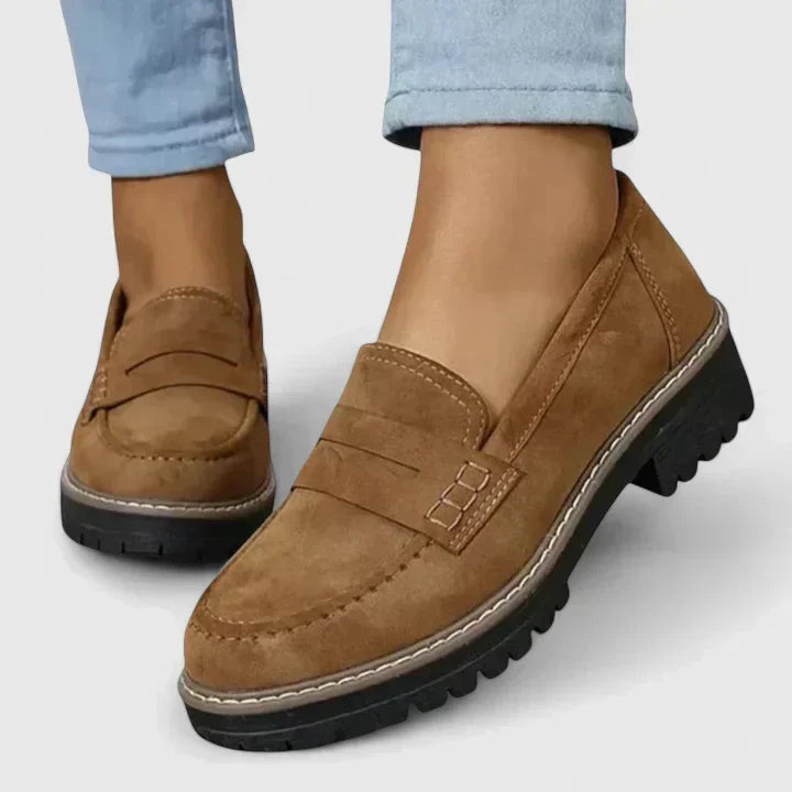 Tan brown suede-look loafers with penny straps and chunky black soles, worn with light blue jeans, detail.