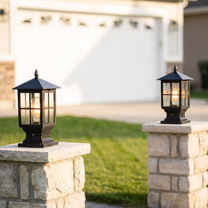 Pair of black glass-paned lanterns glowing on stone pillars in front of a white garage door, with a green lawn between them. 8