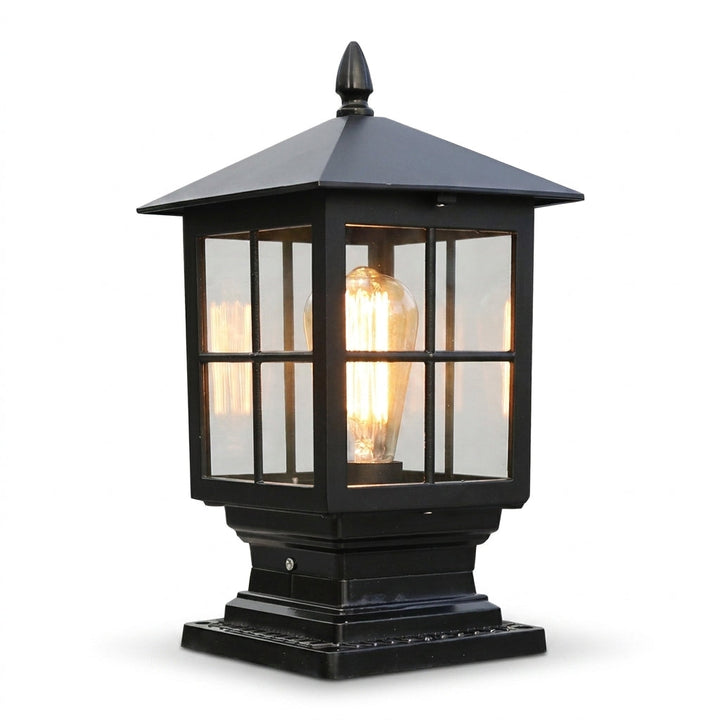 Black square lantern-style pillar lamp with a pyramid roof, finial, glass panes and a glowing filament bulb, on a plain white background. 1