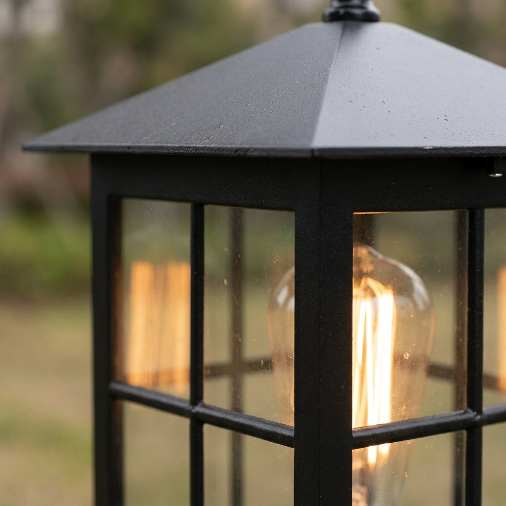 Close-up of the pyramid roof and upper frame of the lamp, with an amber bulb glowing behind the glass panes. 6