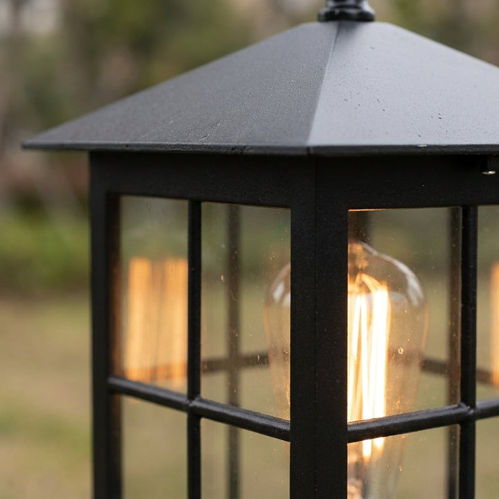 Close-up of the pyramid roof and upper frame of the lamp, with an amber bulb glowing behind the glass panes. 6