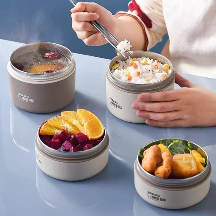 Four round containers on a table holding rice, fruit, soup and fried chicken.