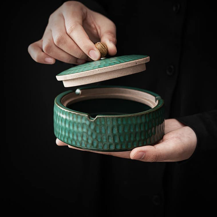 Green textured ceramic ashtray detail with the lid lifted by its wooden knob.