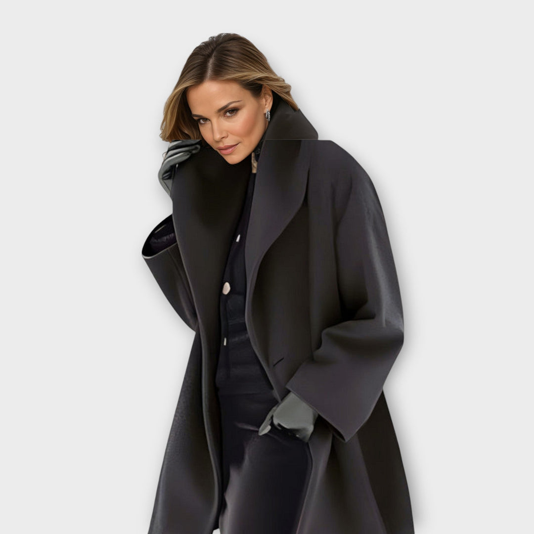 Model wearing the long coat in charcoal black with a broad shawl collar, glancing toward the camera over a dark outfit. 3