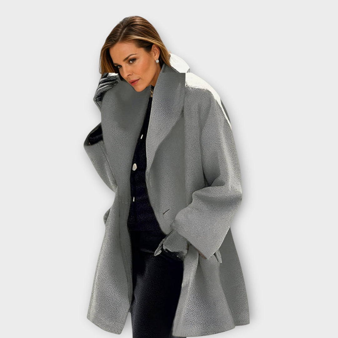 Model wearing the coat in textured gray with a wide open collar over a black outfit, one gloved hand at her collar. 5