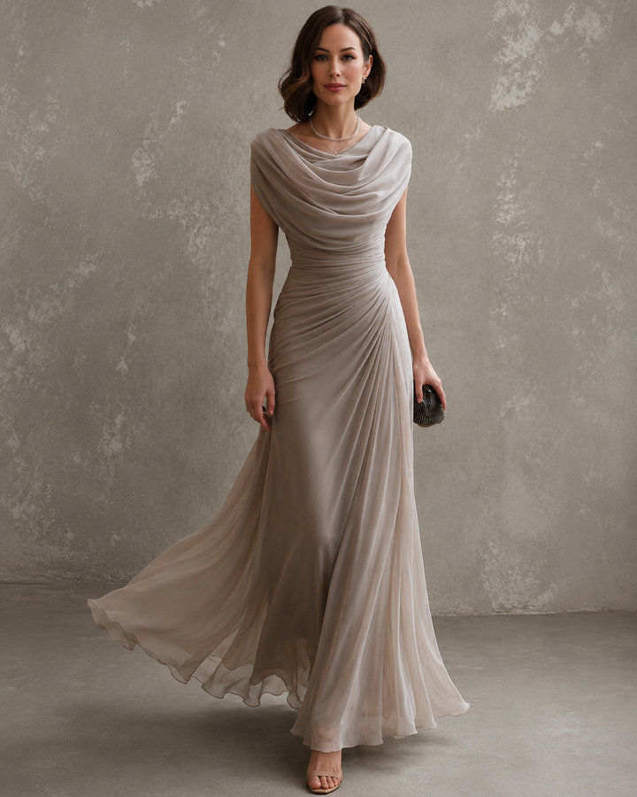Model in the beige dress with a draped cowl neckline, ruched waist and a sheer skirt flowing as she walks.