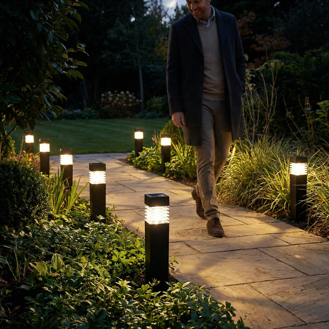 Row of lit black square stake lights lining a stone garden path at dusk.