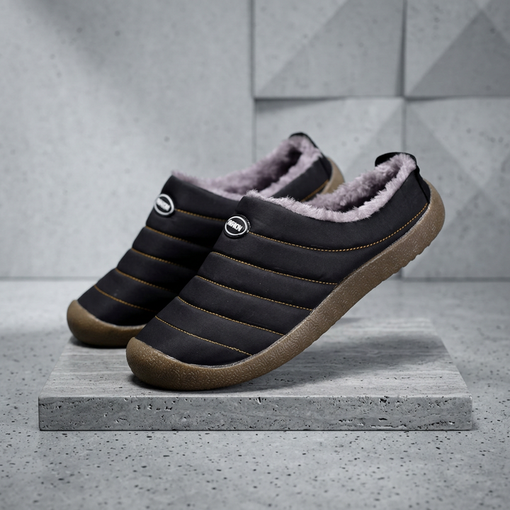 Black quilted slippers with fleece lining, one tilted upright on a stone slab against a concrete wall 19