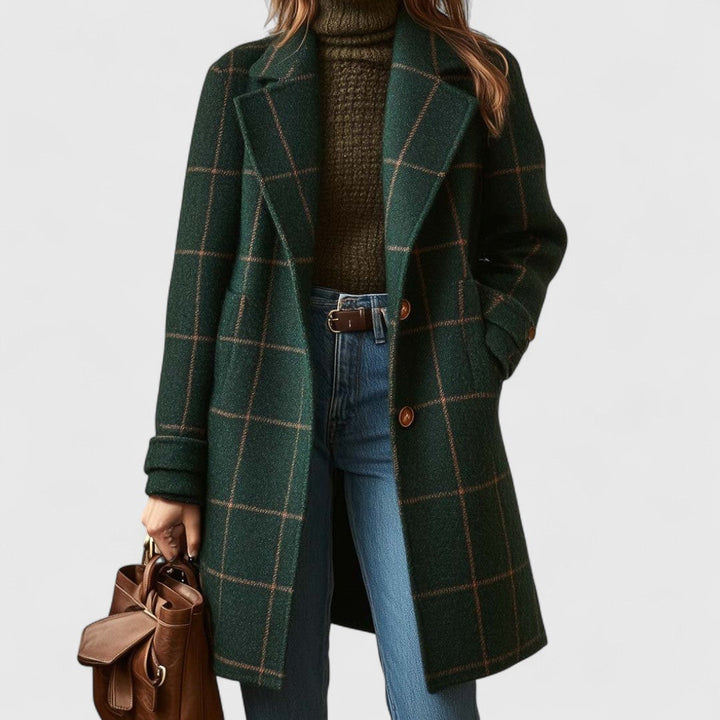 Women's plaid coat in dark green worn open over an olive turtleneck and jeans, with a brown leather handbag.