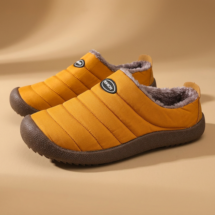 Pair of mustard yellow quilted slippers with brown fleece lining and dark brown soles on a tan studio background 20
