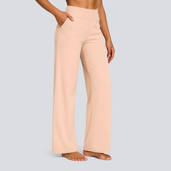 Women's soft peach-beige high-waist wide-leg pants on a model, side view with a hand in the pocket and a patch pocket visible.